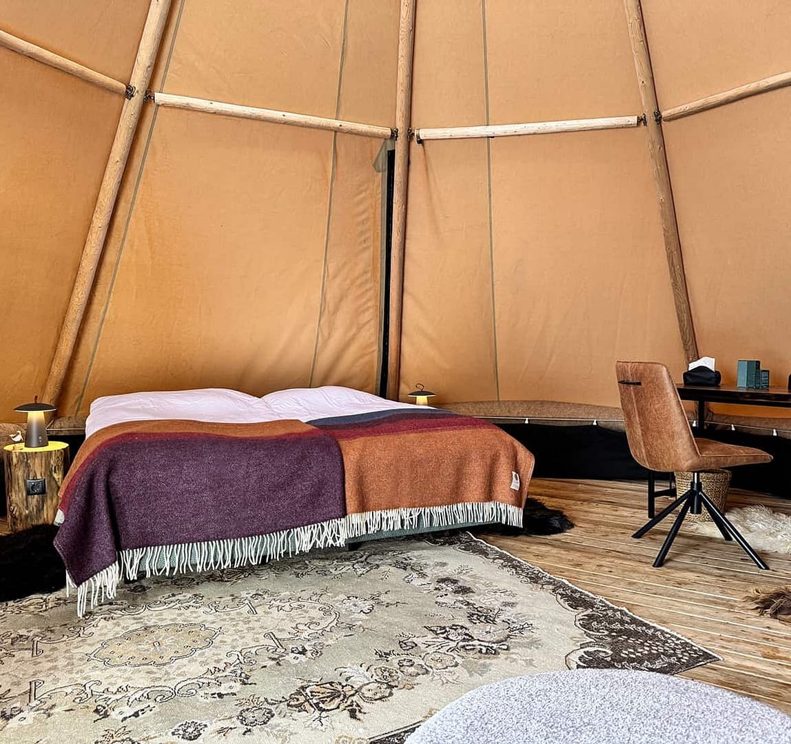 Interior view of a tipi tent with cozy bed and warm lightning